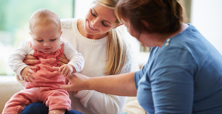 A mother holding a baby on her knee and a health visitor checking the baby