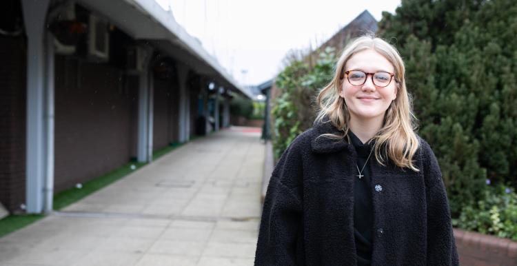 A young woman standing outside a row of buildings and smiling