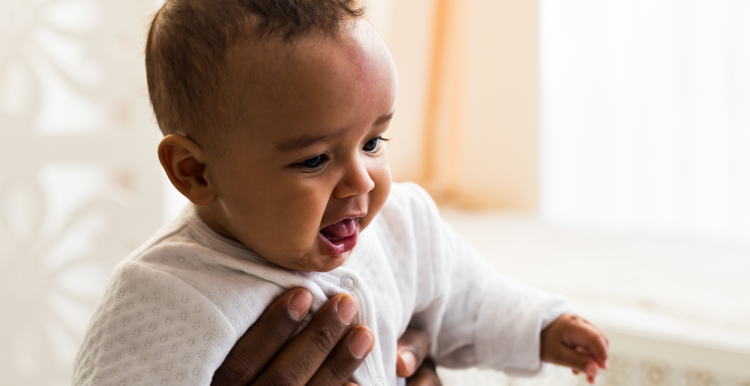 A young Black baby being held up by an adult.