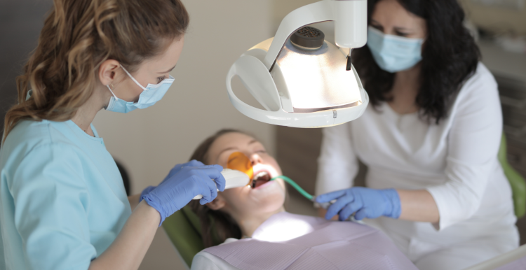 A patient lying on a dentists chair, receiving treatment from two dental professionals.