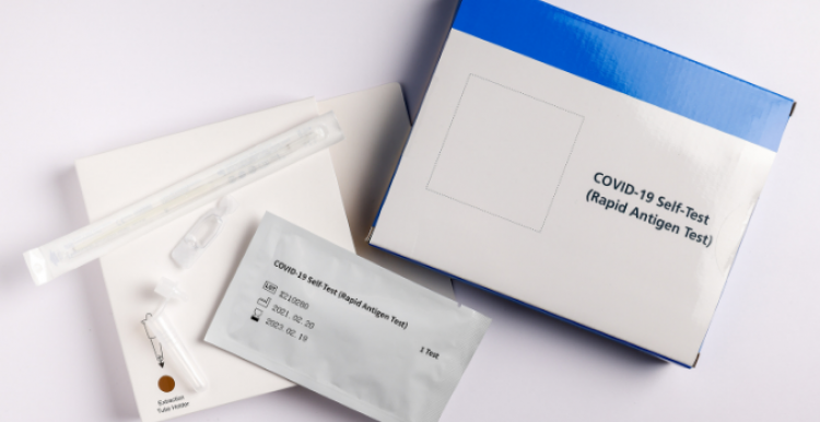 A blue and white box which says: COVID-19 Self Test (Rapid Antigen Test). Around the box is the extraction tube, swab, and test strip in a wrapper