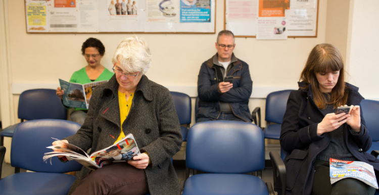 Four people sitting on blue chairs in a waiting room