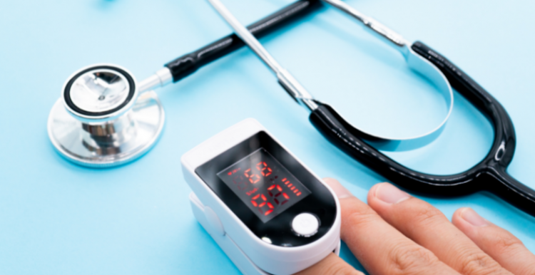 A pulse oximeter on someone's finger with a stethoscope in the background