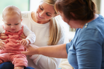 A mother holding a baby on her knee and a health visitor checking the baby