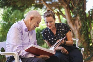 A father and daughter sitting outside, looking at a photo album