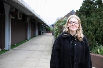 A young woman standing outside a row of buildings and smiling