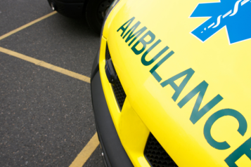 The front of a yellow ambulance, parked in a car park.