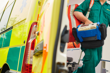 A UK ambulance staff member emerges from the back of an ambulance with his emergency backpack and vital signs monitor.