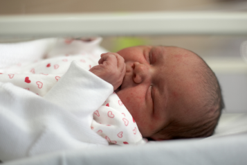 A newborn baby in a cot on a maternity ward.