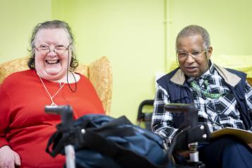 A woman with a walker and a man smiling in a residential setting.