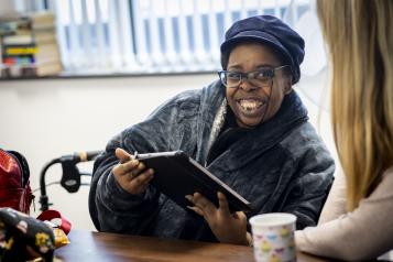 A person with a walker sitting at a table, looking at a tablet.