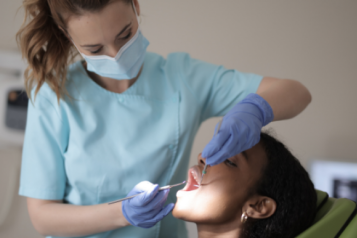 A person sitting in a dentist's chair, having dental work done by a dentist.