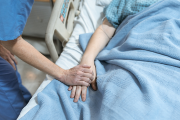 A nurse holding a patient's hand in a hospital bed