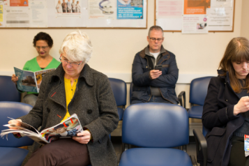 Four people sitting on blue chairs in a waiting room