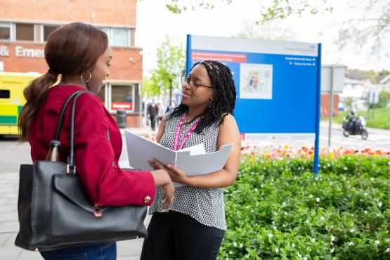 A woman with a clipboard talking to another woman outside a hospital