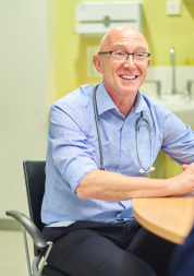 A male GP at his desk, speaking to a female patient.